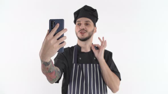 Chef in Uniform Doing Video Call or Online Class on Smartphone Holding It in Hand alt