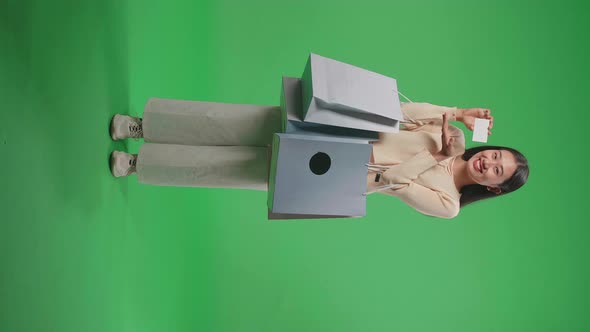 Full View Of An Asian Woman With Shopping Bags Holding A White Card And Smile On Green Screen alt
