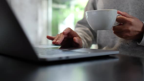 Closeup a woman drinking coffee while working and touching on laptop computer touchpad