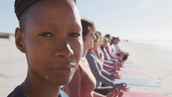 Multi-ethnic group of women doing yoga position and African American looking at camera on the beach alt