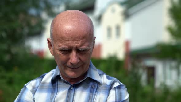 Elderly Bald Man Is Sitting and Resting Outdoors at Summer Day alt