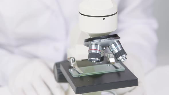 Female Lab Technician in Rubber Gloves Adjusts Focus of Microscope Close Up