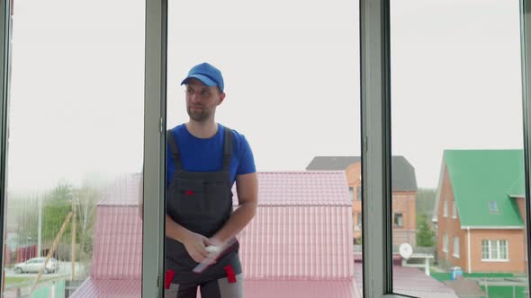 Handyman in Uniform Cleans Windows in Cottage Outdoors alt