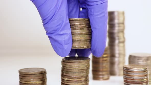 A hand in medical gloves puts coins into a column. Investment concept
