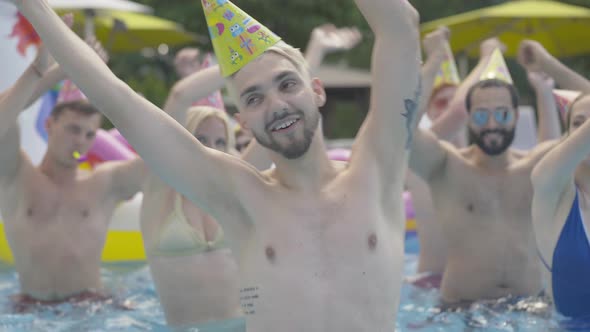 Close-up of Cheerful Young Tattooed Man with Blond Dyed Hair Dancing and Spinning in Water at Resort alt