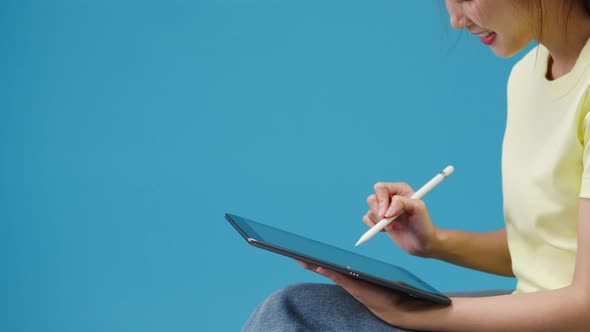 Young girl using digital tablet looking at empty space isolated over blue background.