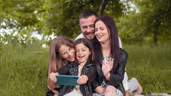Cheerful Parents and Their Cute Daughters Sitting Together on Green Grass and alt