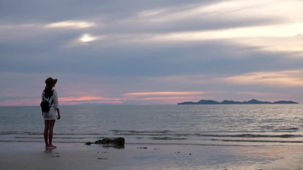 rear view of a woman with hat standing and looking at the sea before sunset