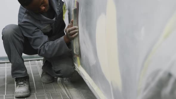 African American male car mechanic working in a township workshop and polishing a side of a car alt