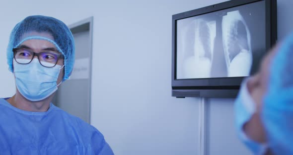 Asian surgeon wearing surgical cap and face mask discussing x ray with colleagues alt