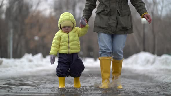 Mom and Daughter Walking in a Puddle in Yellow Rubber Boots