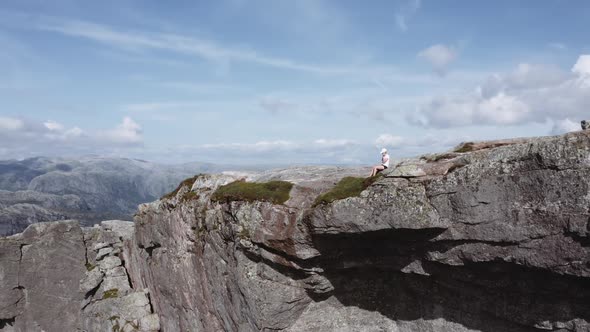 Aerial Shot of a Woman Sitting By the Edge of a Cliff at Pulpit Rock alt