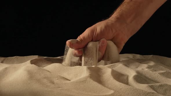 Male Hand Squeezing and Spilling a Handful of Dry Sand on Black Studio Background alt