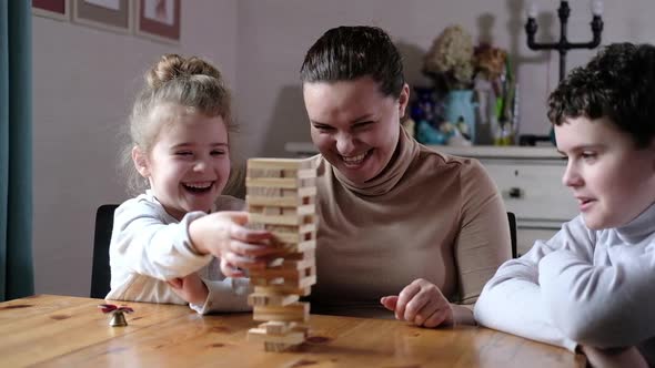 playful mom helps preschool children build tower of wooden blocks in living room alt