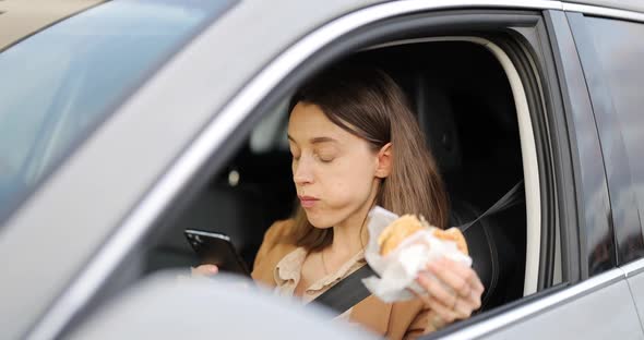 Woman Typing on a Smart Phone While Having a Snack in a Vehicle alt