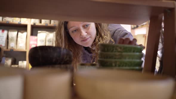 Young Woman Takes Bowls Standing on Shelf in Supermarket alt