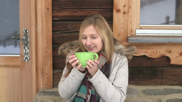 Young woman sitting outside chalet and drinking coffee