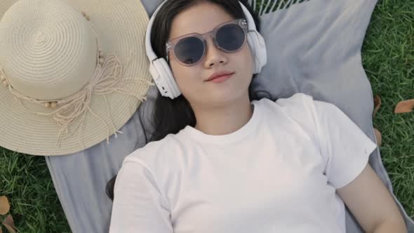 Smiling of Asian female wearing sunglasses and headphones while lying on the floor grass.