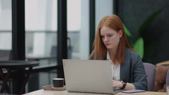 A Young Redhaired Woman is Working on a Laptop alt