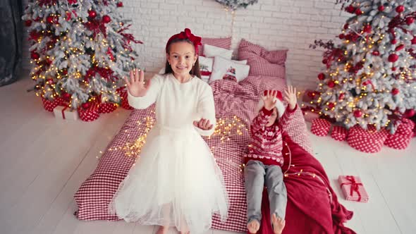 Portrait of Attractive Cute Kids Wearing Christmas Wear Falling Together on Bed in Apartment alt