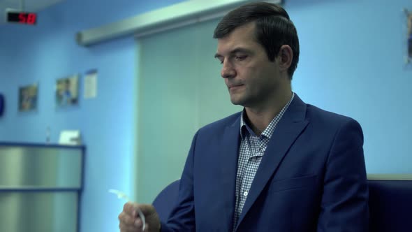 Mature Man Sit with Ticket Number in Queue alt