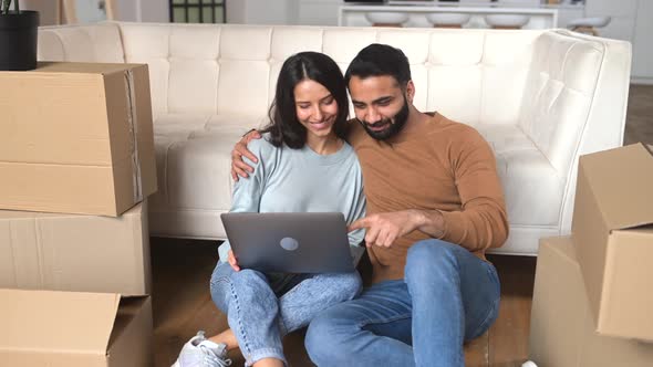 Lovely Indian Couple Choosing New Furniture Online in New House Sitting on the Floor