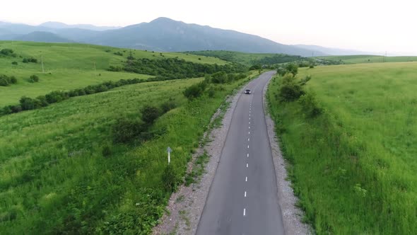 panorama of the mountain landscape. a black car is driving along the road. alt