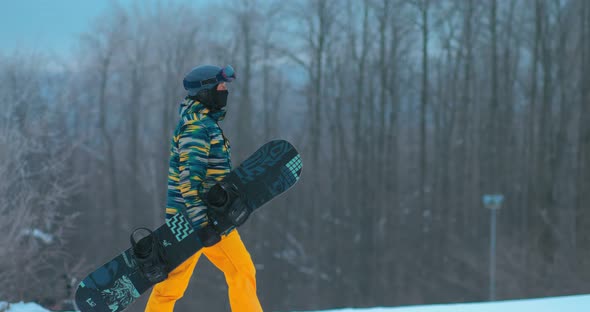 Snowboarder Athlete Goes Uphill in the Snow and Holds a Snowboard in His Hands. Snowboarding Goes alt