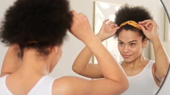 African american black woman styling curly afro hair. Makes hairstyle with hair band accessory alt