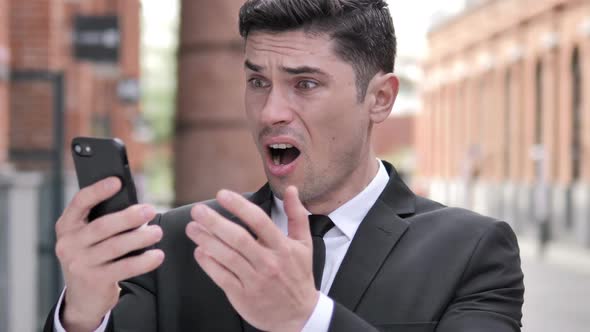 Outdoor Businessman Reacting to Loss Using Smartphone alt