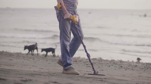 Unrecognizable Man with Electronic Metal Detector Scanning Sand on the Beach with Metal Detector alt