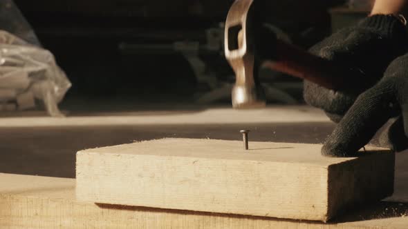 A Male Construction Worker Hammers a Nail Into a Board with a Hammer