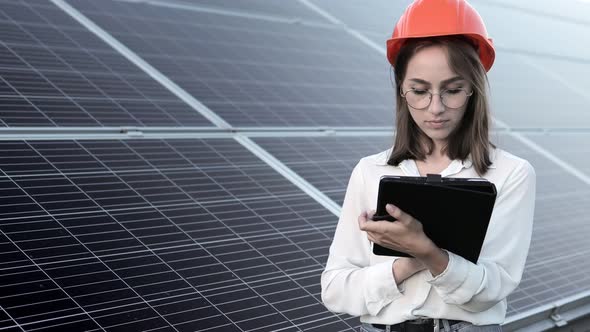 Beautiful young engineer standing near solar panels outdoors, Green Energy Concept. alt