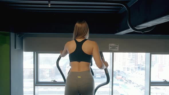 Back View of Young Woman During Cardio Workout on an Elliptical Trainer Alone