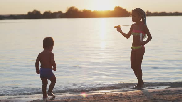 Naked Boy Catches Bubbles on the Beach of the Lake That His Sister Lets alt