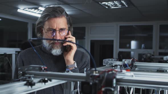 Middle Aged Designer Speaking on Smartphone Near 3D Printer alt