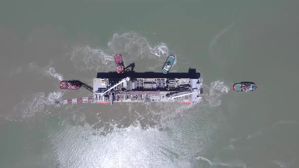 Aerial view of cargo ship arriving at the port with the help of tugs. alt