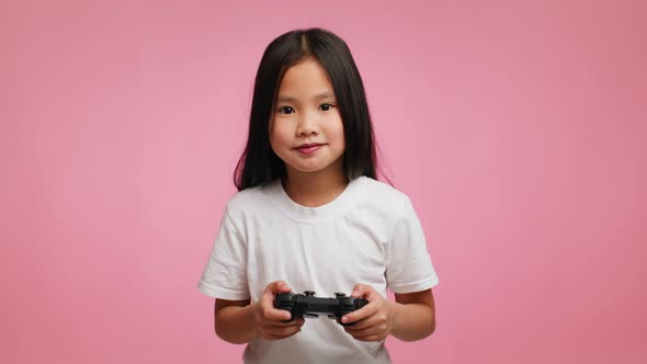 Excited Japanese Little Girl Playing Videogame Standing Over Pink Background alt