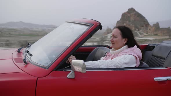 Happy Woman is Sitting in Retro Red Convertible Car Among Rocks