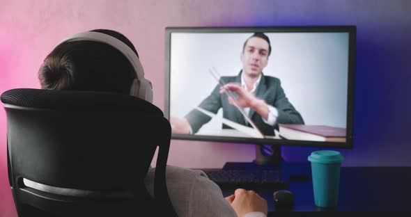 Rear View of a Young Man with Headphones Watching a Video Blog Indoors alt