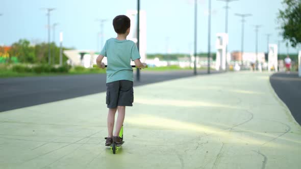 Boy Riding a Children's Scooter on City Street on Weekend alt