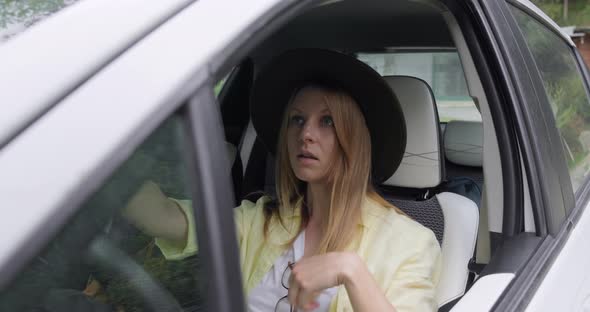 Young traveler woman sitting in car and fixing her hat in mirror. alt