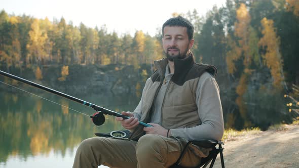 Slow Motion Portrait of Young Man Catching Fish and Looking at Camera Outdoors in River Bank alt