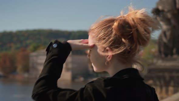 Woman Shielding Eyes From Sun As She View River From Charles Bridge alt