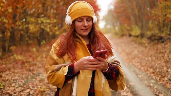 Active Caucasian Female Walking Along with Headphones Using Mobile Phone Enjoys Nature in a City alt