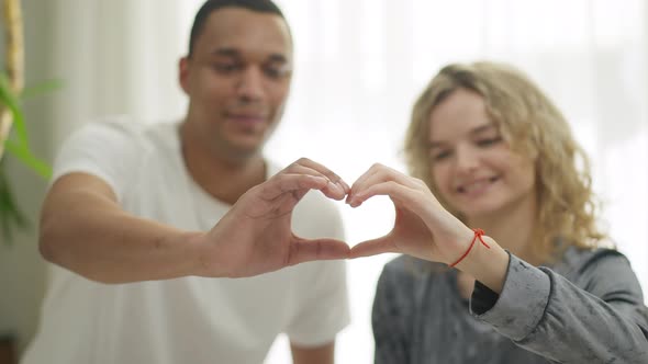 Closeup Hands of Young Interracial Loving Happy Couple Making Heart Shape with Blurred Smiling alt