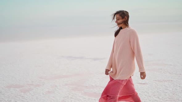 Walking Girl in Big Sweater and Blowing Pink Dress at Beautiful Landscape of Salt Flats at Pink Lake alt