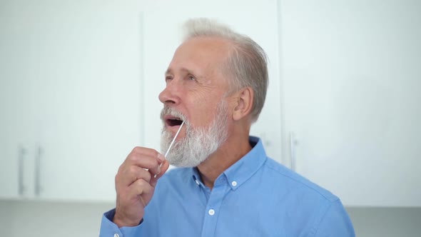 Closeup of Mature Caucasian Adult Man Taking Swab Sample of Mouth Carrying Out Coronavirus Self Home alt