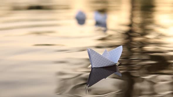 A paper boat is floating on the waves in the water at a beautiful sunset. homemade Origami boats