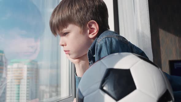 Caucasian Boy on a Home Quarantine Looking Out the Window a Bored Boy Holds a Soccer Ball alt